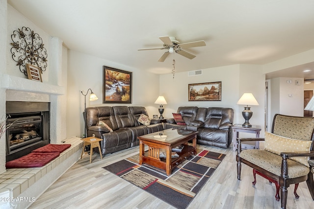 living room featuring a large fireplace, ceiling fan, and light wood-type flooring