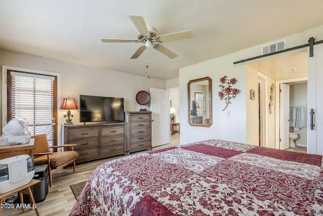 bedroom featuring connected bathroom, light hardwood / wood-style flooring, a barn door, and ceiling fan