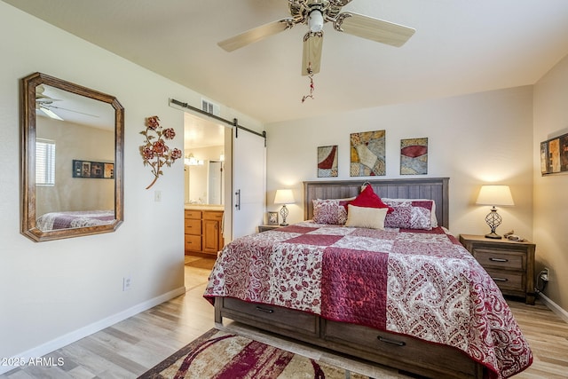 bedroom with ensuite bath, light hardwood / wood-style flooring, a barn door, and ceiling fan