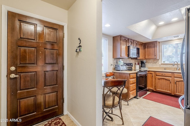 kitchen featuring sink, light tile patterned floors, a tray ceiling, decorative backsplash, and stainless steel electric stove