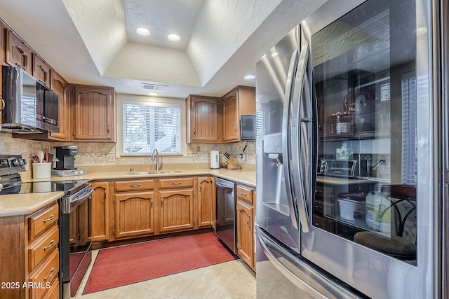 kitchen featuring sink, light tile patterned floors, stainless steel appliances, tasteful backsplash, and a tray ceiling