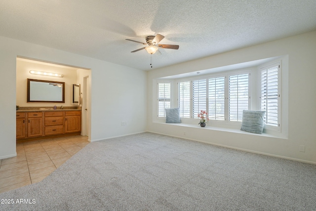 unfurnished bedroom with baseboards, light colored carpet, a sink, and ensuite bath