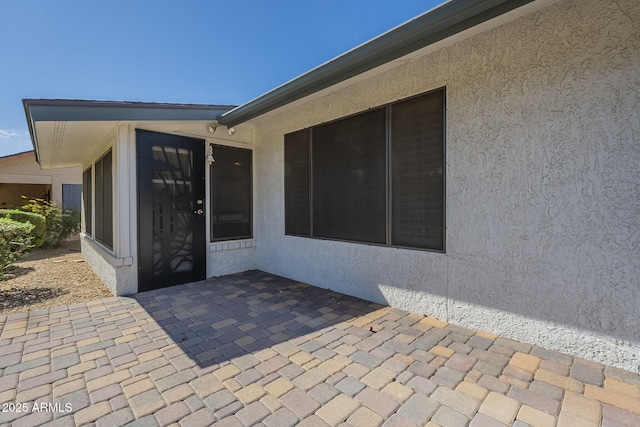 view of exterior entry featuring stucco siding and a patio area