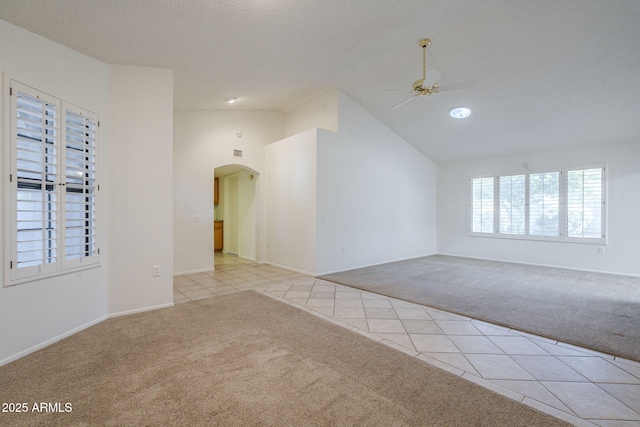 empty room with arched walkways, a ceiling fan, light tile patterned flooring, and light colored carpet