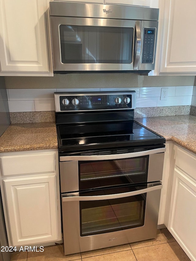 kitchen featuring light stone countertops, light tile patterned flooring, appliances with stainless steel finishes, and white cabinetry