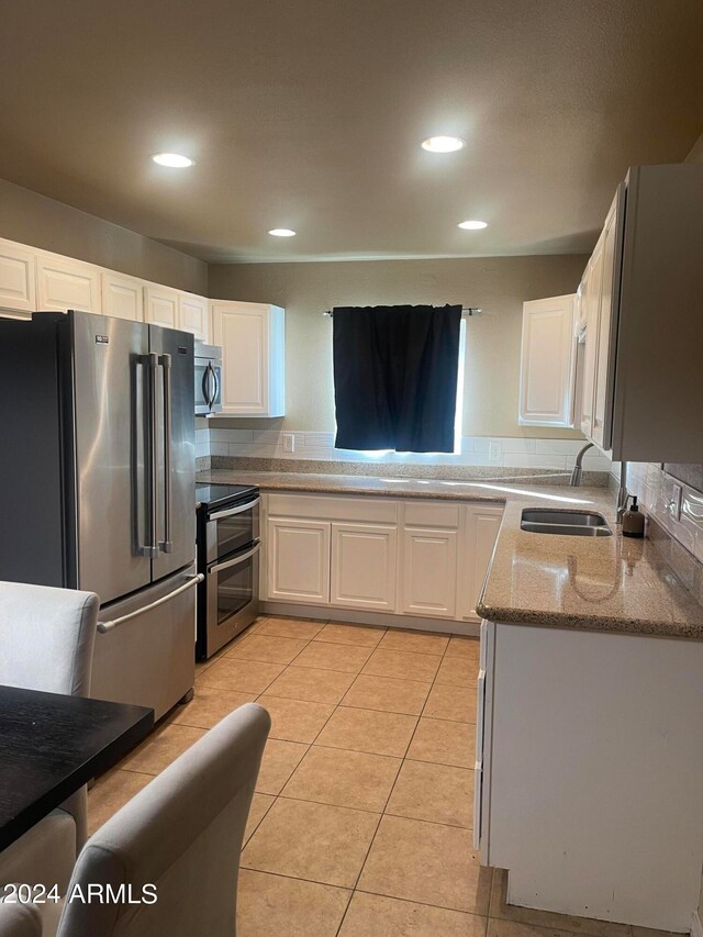 kitchen with light stone counters, stainless steel appliances, sink, light tile patterned flooring, and white cabinetry