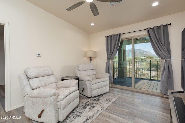 sitting room with light wood-type flooring, ceiling fan, and a mountain view