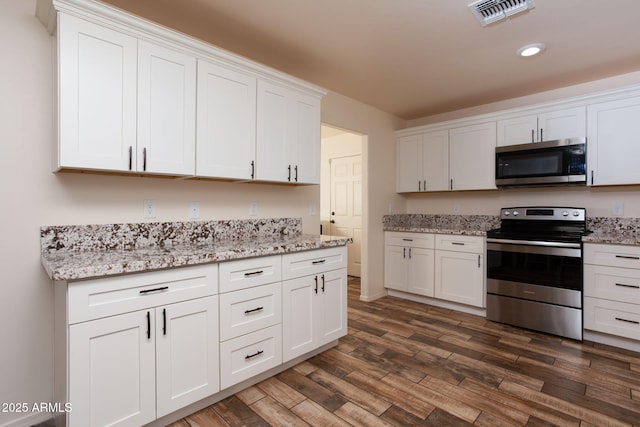 kitchen with dark wood-type flooring, white cabinets, appliances with stainless steel finishes, and light stone counters