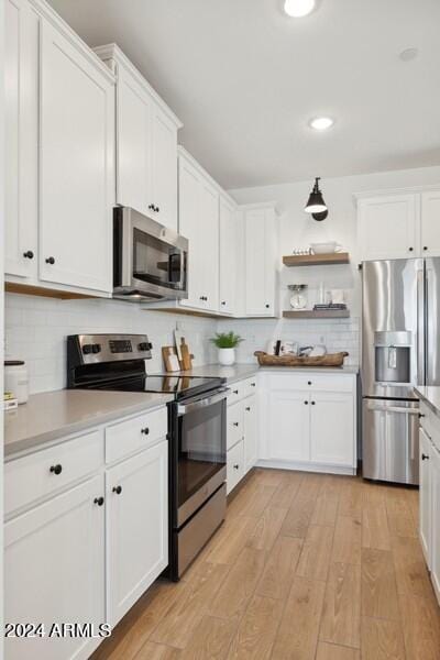 kitchen with white cabinets, appliances with stainless steel finishes, light wood-type flooring, and tasteful backsplash