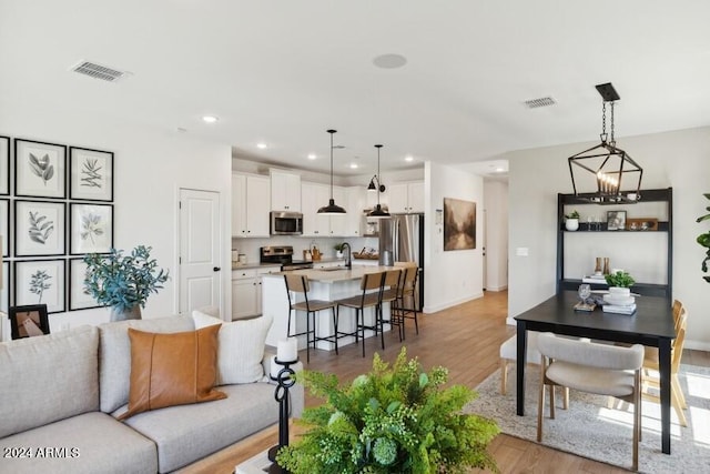 living room with a notable chandelier, sink, and light hardwood / wood-style flooring