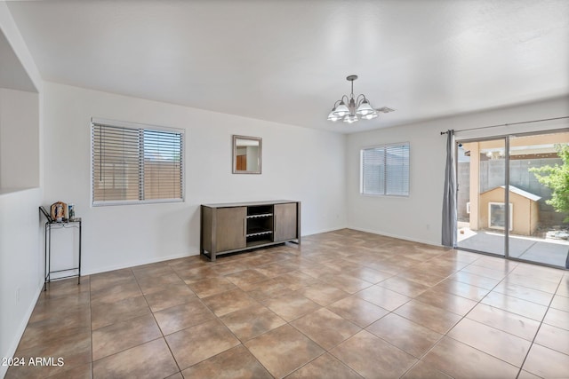 tiled spare room featuring baseboards and a notable chandelier