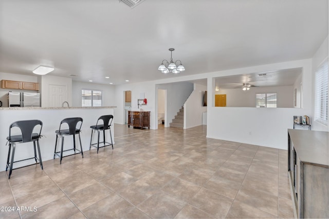 kitchen featuring light stone counters, decorative light fixtures, stainless steel refrigerator with ice dispenser, light brown cabinetry, and open floor plan