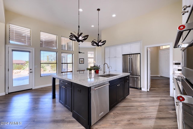 kitchen with a center island with sink, stainless steel appliances, sink, hardwood / wood-style flooring, and white cabinets