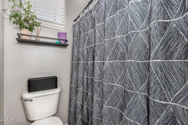 full bathroom featuring curtained shower, toilet, and a textured wall