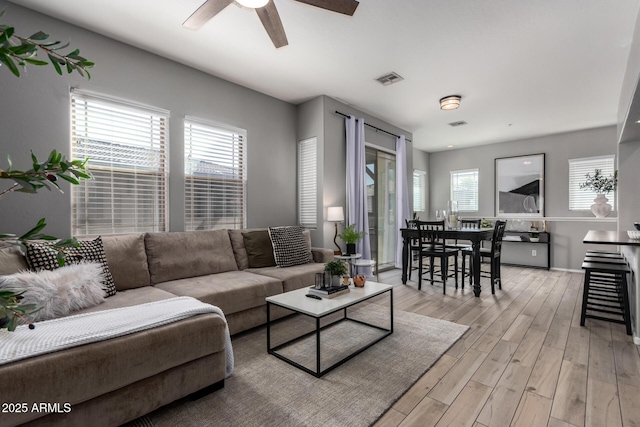 living room featuring plenty of natural light, light wood-style flooring, visible vents, and ceiling fan