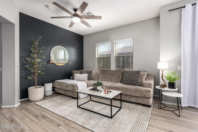 living room with baseboards, a ceiling fan, wood finished floors, and an accent wall