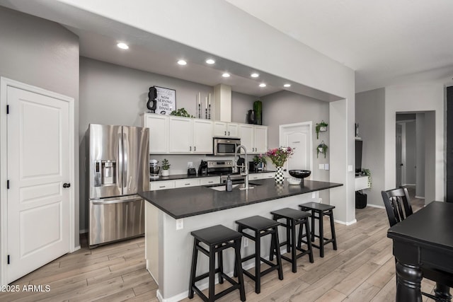 kitchen with a sink, light wood-style floors, appliances with stainless steel finishes, white cabinetry, and dark countertops