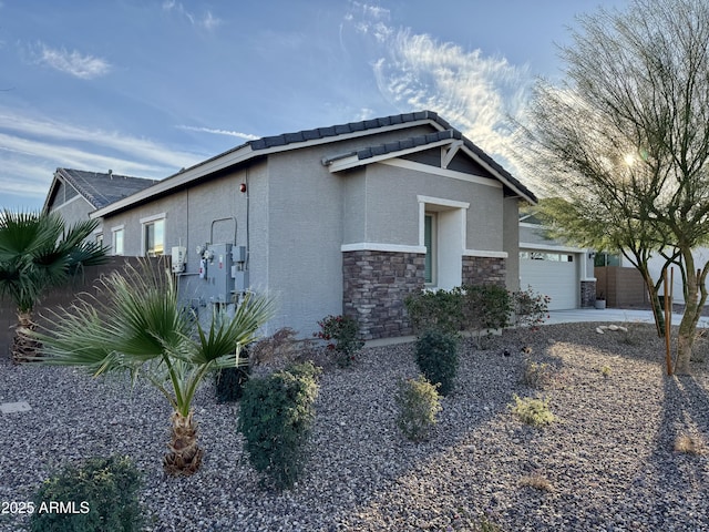 view of home's exterior with an attached garage, stone siding, fence, and stucco siding