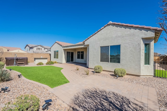 rear view of house with a patio, stucco siding, a hot tub, fence private yard, and a tiled roof