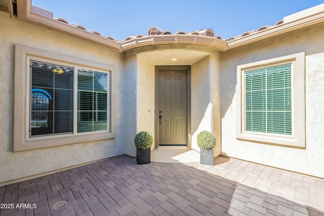 property entrance featuring a tile roof, a patio area, and stucco siding