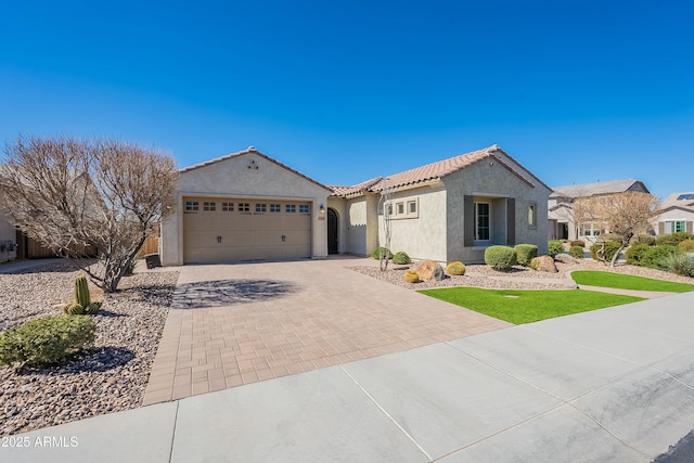 mediterranean / spanish-style house featuring decorative driveway, a tile roof, an attached garage, and stucco siding