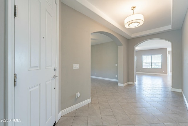 unfurnished room with arched walkways, a raised ceiling, light tile patterned flooring, and baseboards