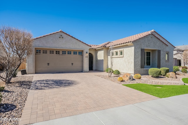 mediterranean / spanish house with a garage, a tiled roof, decorative driveway, and stucco siding