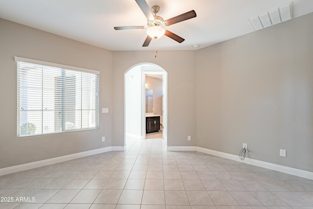 empty room with arched walkways, light tile patterned floors, visible vents, baseboards, and a ceiling fan