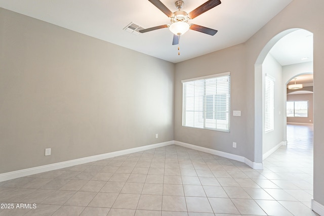 unfurnished room with arched walkways, light tile patterned floors, visible vents, ceiling fan, and baseboards