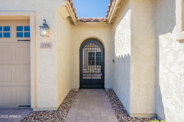 entrance to property featuring an attached garage, a tile roof, and stucco siding