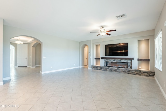 unfurnished living room featuring visible vents, a ceiling fan, light tile patterned flooring, a stone fireplace, and baseboards