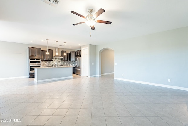 unfurnished living room with arched walkways, visible vents, ceiling fan, and baseboards