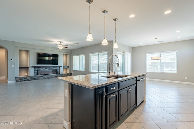 kitchen with arched walkways, a sink, open floor plan, hanging light fixtures, and an island with sink