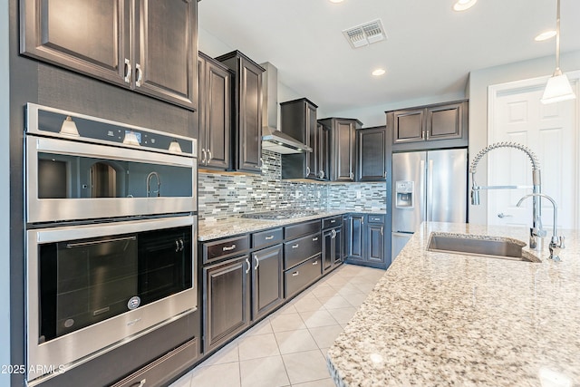 kitchen featuring stainless steel appliances, visible vents, hanging light fixtures, a sink, and wall chimney range hood