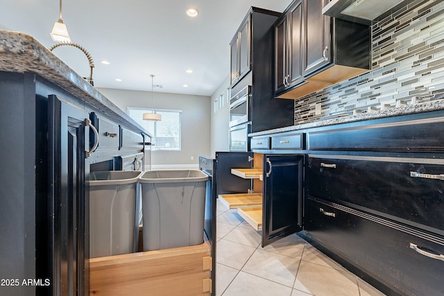 kitchen with light tile patterned floors, tasteful backsplash, hanging light fixtures, wall chimney range hood, and oven