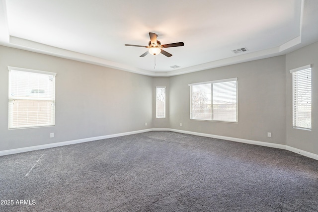 empty room featuring ceiling fan, a raised ceiling, visible vents, and baseboards