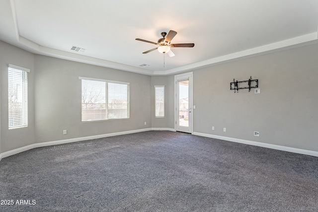 unfurnished room featuring a tray ceiling, visible vents, dark carpet, and baseboards