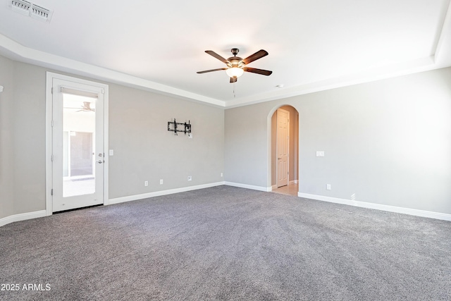 carpeted empty room featuring baseboards, visible vents, arched walkways, a ceiling fan, and a tray ceiling