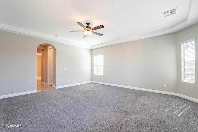 carpeted empty room featuring arched walkways, visible vents, ceiling fan, and baseboards