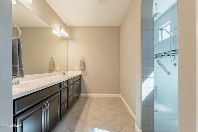 bathroom featuring double vanity, a sink, tile patterned flooring, tiled shower, and baseboards