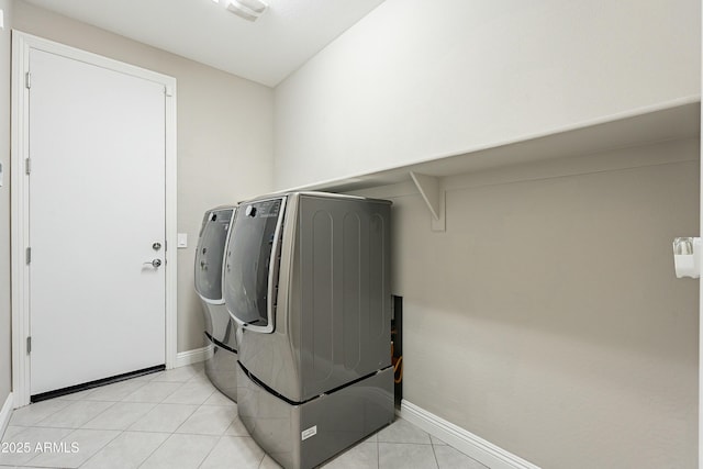 washroom with light tile patterned floors, laundry area, washing machine and clothes dryer, and baseboards