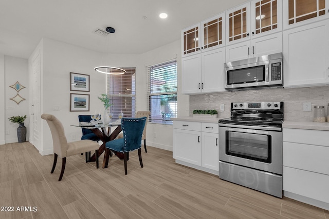 kitchen featuring decorative backsplash, white cabinetry, appliances with stainless steel finishes, and light hardwood / wood-style flooring