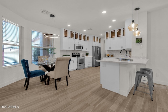 kitchen with hanging light fixtures, kitchen peninsula, light hardwood / wood-style floors, white cabinets, and appliances with stainless steel finishes