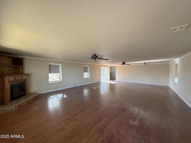 unfurnished living room with dark wood-style floors, visible vents, ornamental molding, and a glass covered fireplace