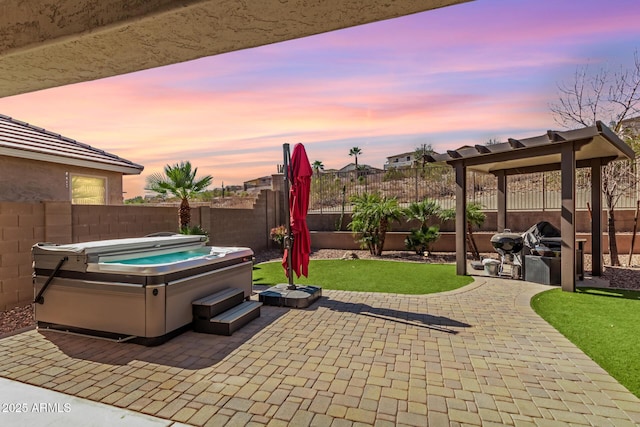 patio terrace at dusk with a fenced backyard, a lawn, and a hot tub