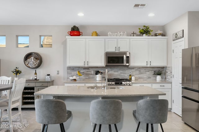 kitchen featuring stainless steel appliances, an island with sink, visible vents, and white cabinetry