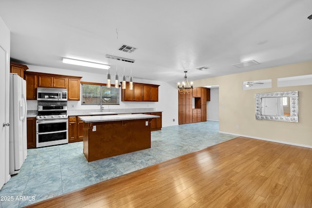 kitchen featuring a center island, stainless steel appliances, hanging light fixtures, a notable chandelier, and light hardwood / wood-style flooring