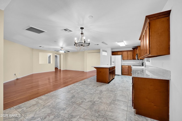 kitchen featuring decorative light fixtures, a center island, sink, white refrigerator with ice dispenser, and ceiling fan with notable chandelier