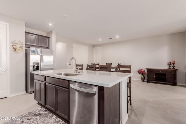 kitchen featuring dark brown cabinetry, sink, stainless steel appliances, an island with sink, and a breakfast bar