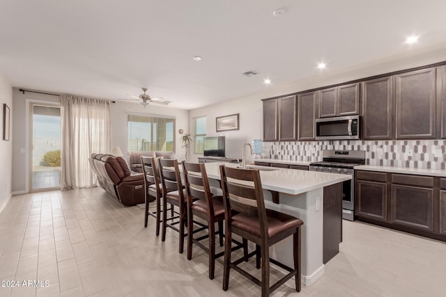 kitchen with a kitchen bar, backsplash, stainless steel appliances, a kitchen island with sink, and sink